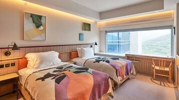 A hotel room with two beds, a desk, a chair, a window with a view, and artwork on the walls.