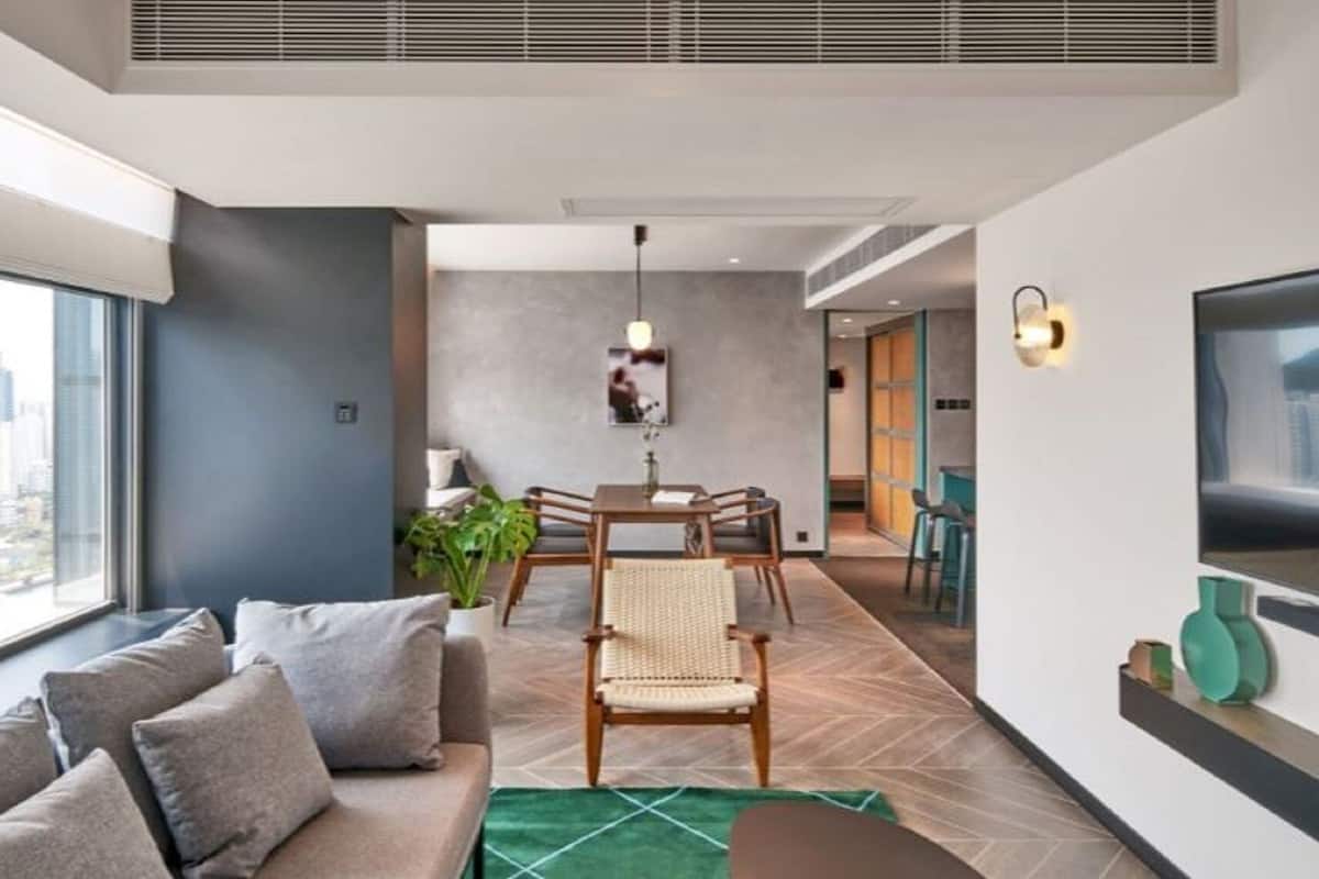 A modern living room with a sofa, dining table, and chairs, a large window with a city view, and a TV mounted on the wall.
