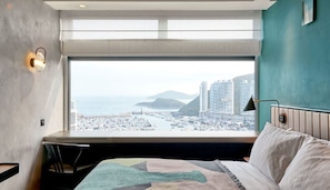 Ein Hotelzimmer mit groĂem Fenster und Blick auf Strand und Stadtlandschaft.