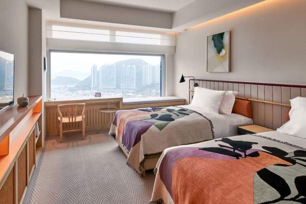 A hotel room with a bed, a desk, a chair, a TV, and a large window with a city view.