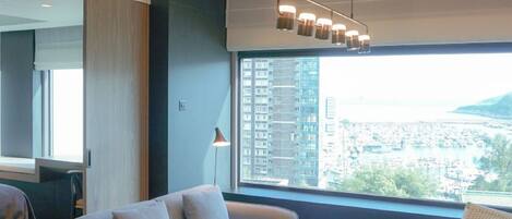 A modern hotel room with a large window, a sofa, a lamp, and a ceiling light fixture.