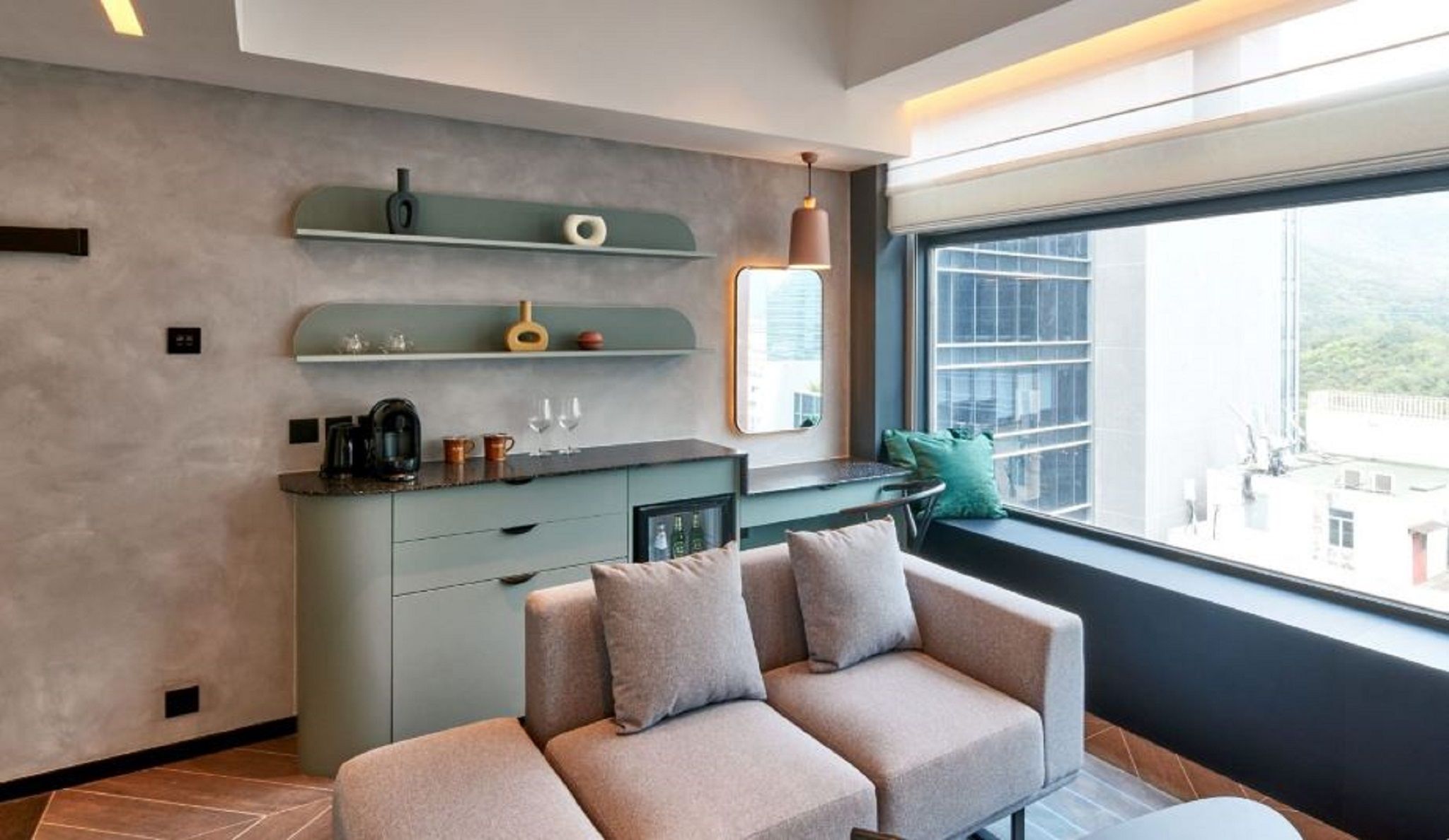 A modern living space with a sofa, a kitchen area with a coffee machine, and a large window offering a view.