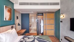 A modern hotel room with a bed, a desk, a shower area, and a TV.