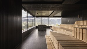 A modern interior with a long, narrow room featuring a fireplace, large windows, and a wooden bench area. - Santre dolomythic home (Bressanone)
