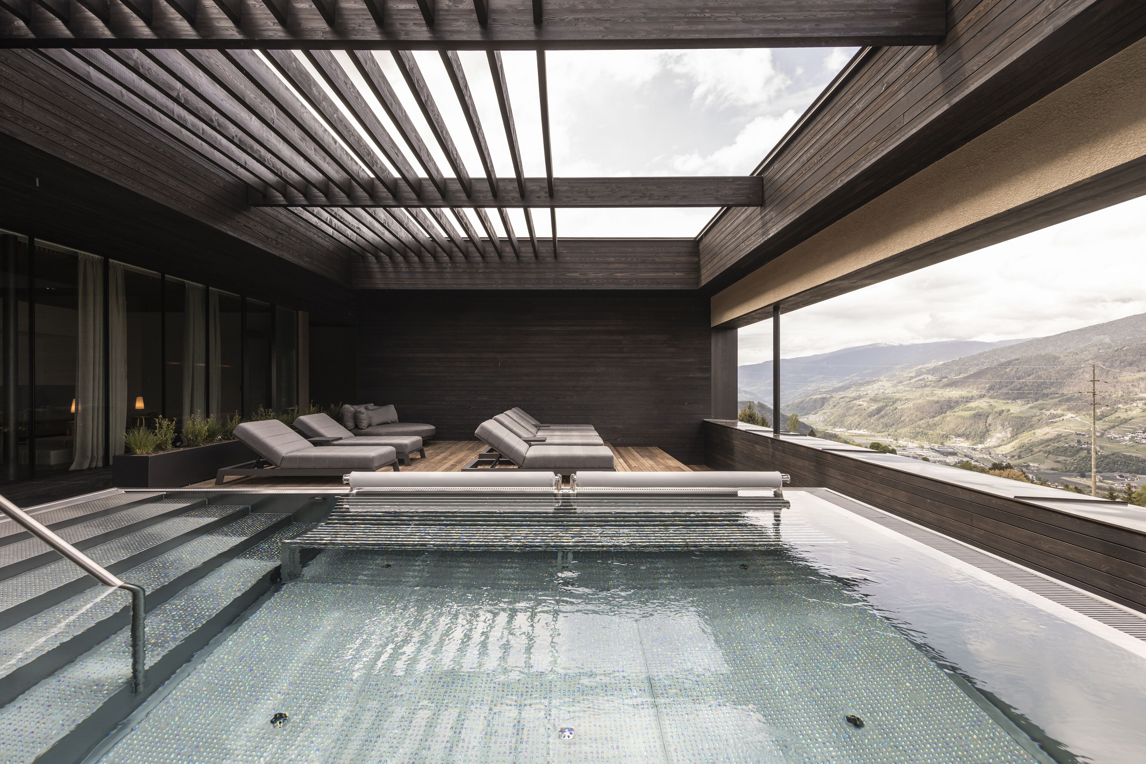 A modern indoor pool area with a skylight, lounge chairs, and a view of the mountains.