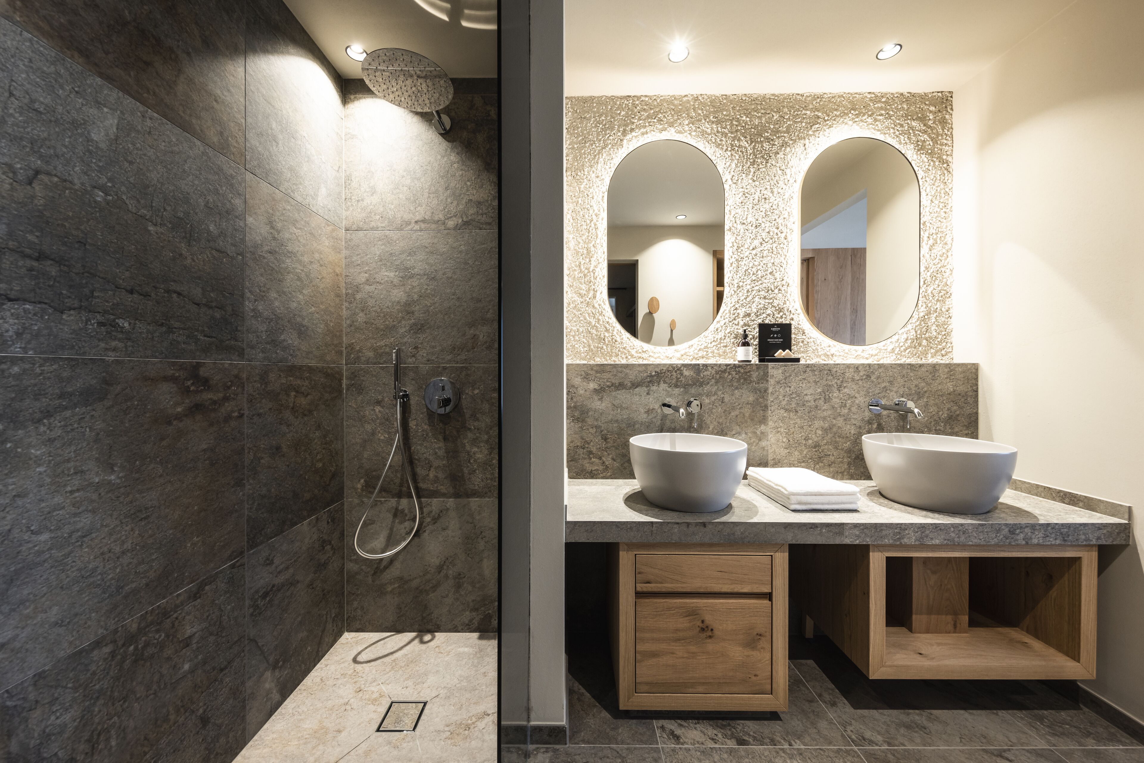 A modern bathroom with a large mirror, two sinks, and a shower area.