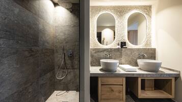 A modern bathroom with a large mirror, two sinks, and a shower area.