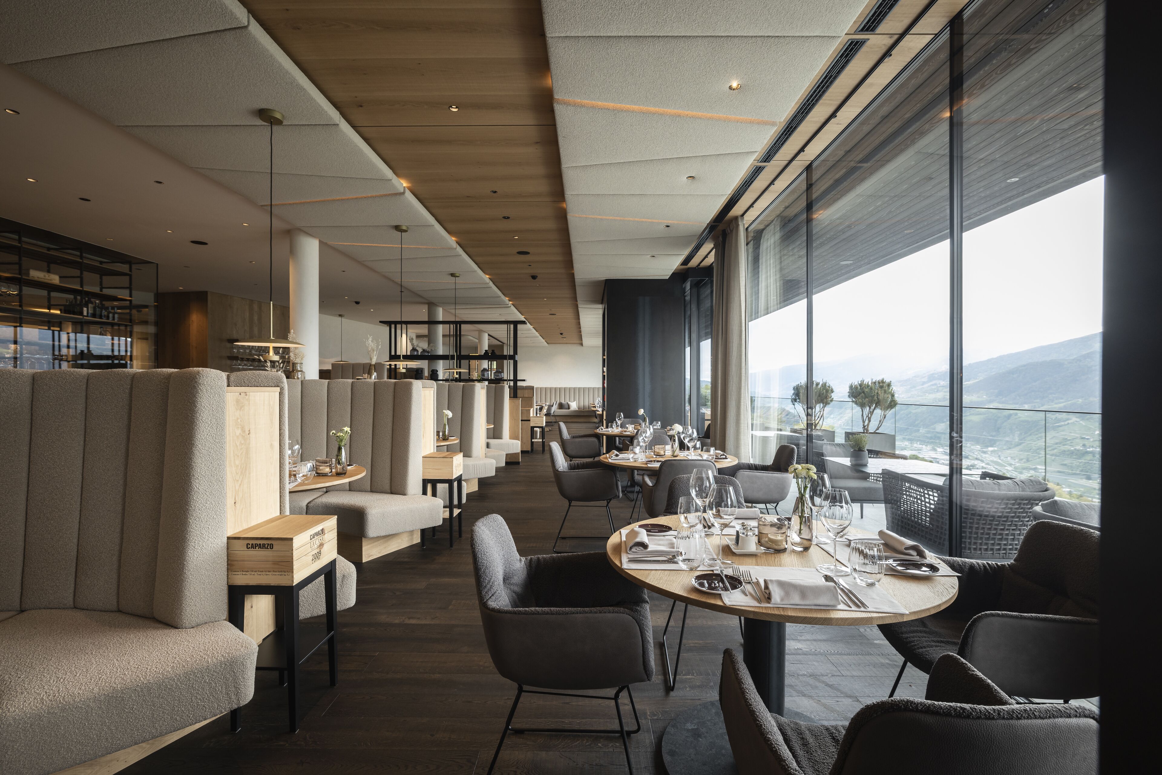 Un restaurant modern amb taules altes i seients, grans finestres que ofereixen una vista de la ciutat i les muntanyes.