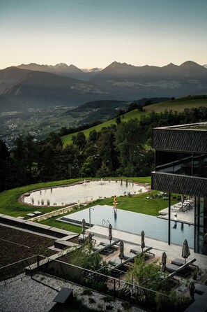 A modern building with a rooftop pool, surrounded by lush greenery and mountains in the background.