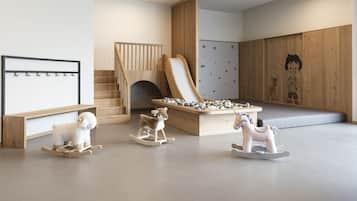 Une salle de jeux avec un toboggan en bois, un mur d’escalade et des chevaux à bascule.