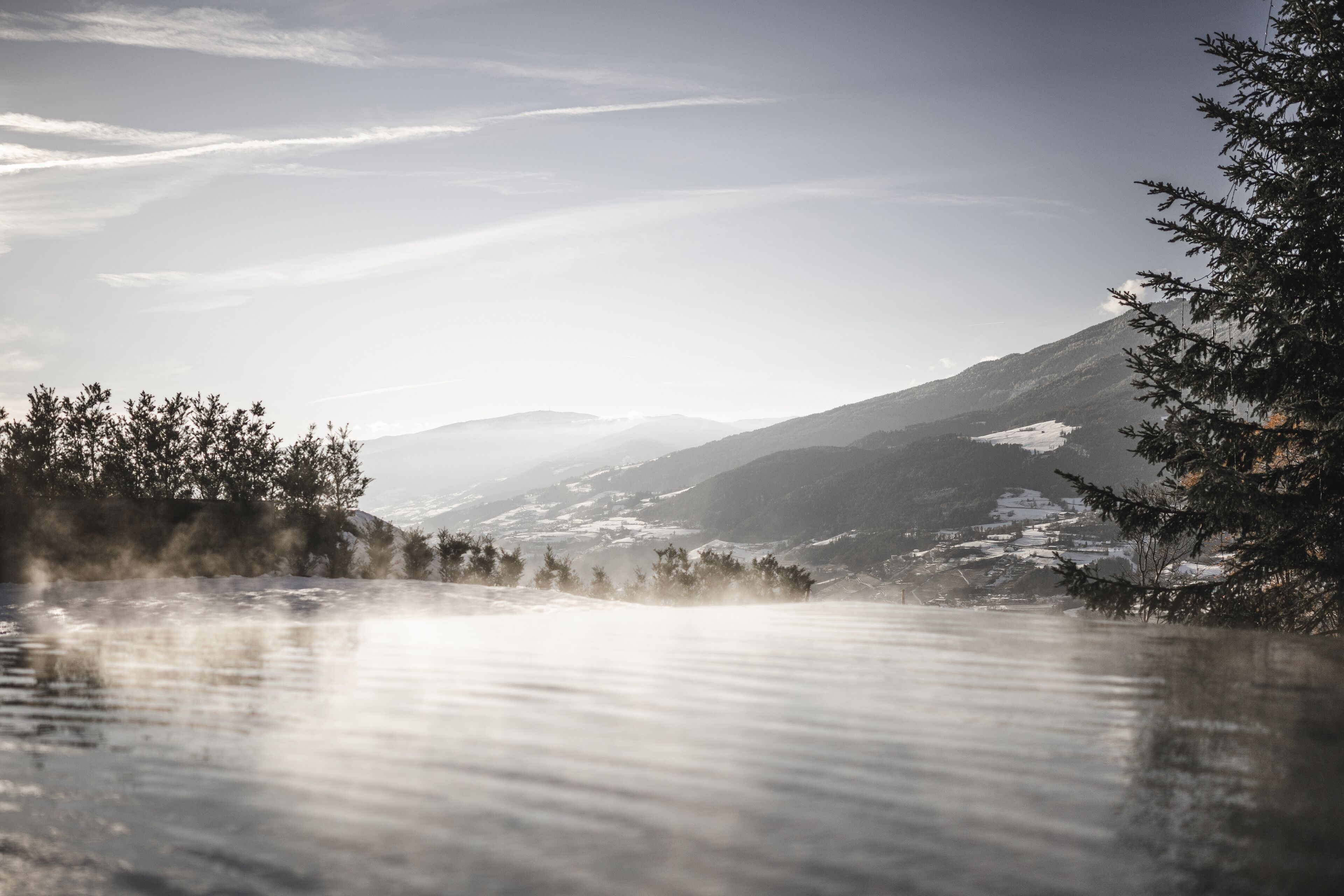 A serene landscape with a mountain range in the background, a body of water in the foreground, and trees framing the scene.