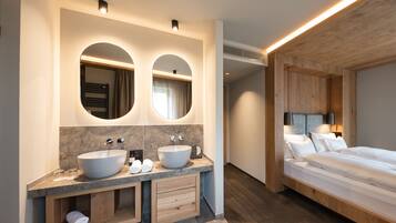 Un baño moderno con lavamanos doble, tocador y un dormitorio independiente con cama y mesita de noche.