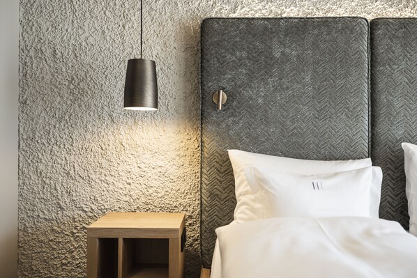 A bed with white linens, a textured wall, and a small wooden nightstand. - Santre dolomythic home (Bressanone)