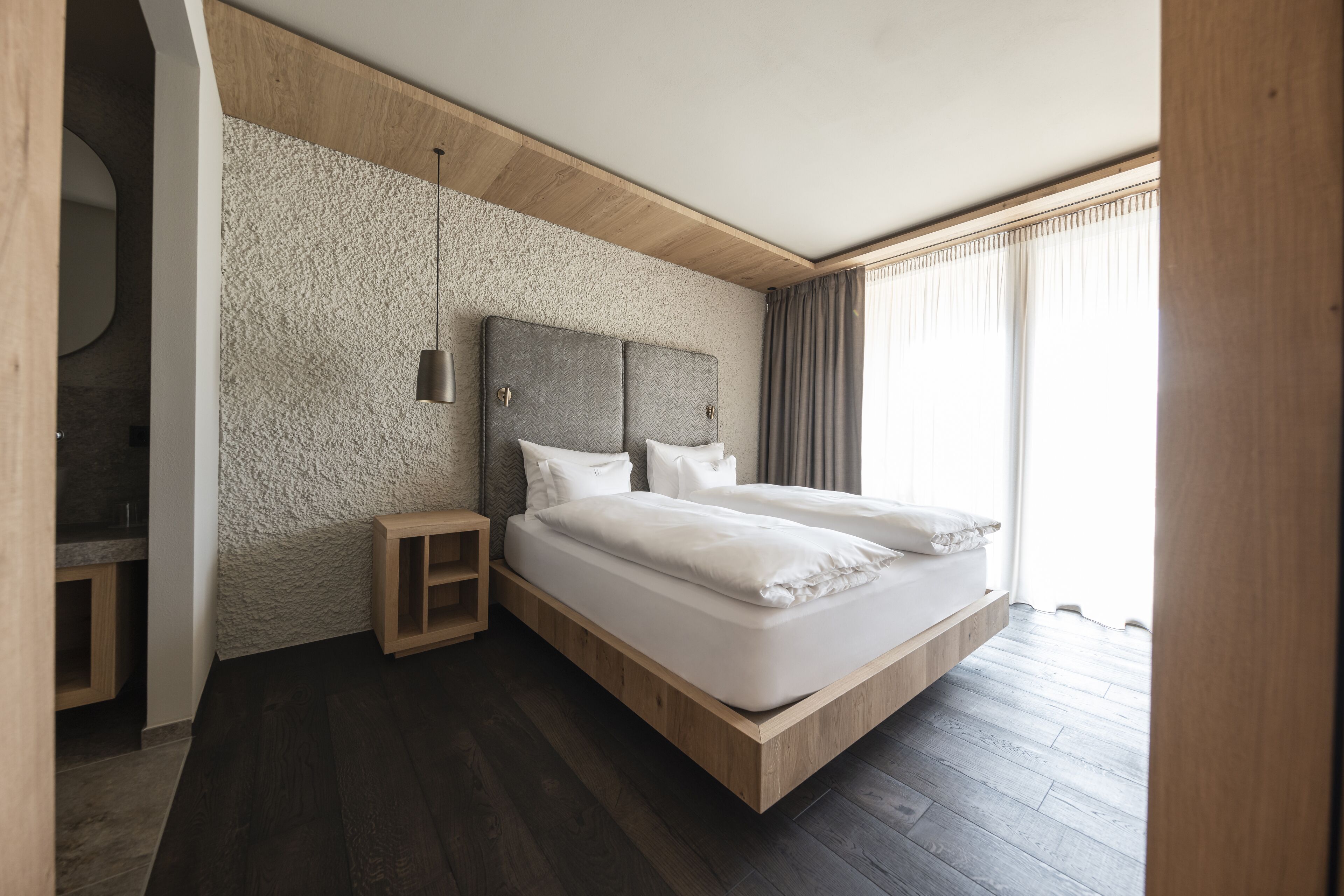 Un dormitorio moderno con cama empotrada, una mesita de noche pequeña y un ventanal con cortinas.