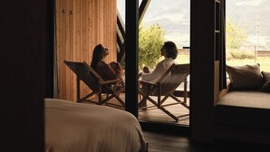 Una habitación con una cama, dos sillones y vistas a las montañas a través de un gran ventanal.