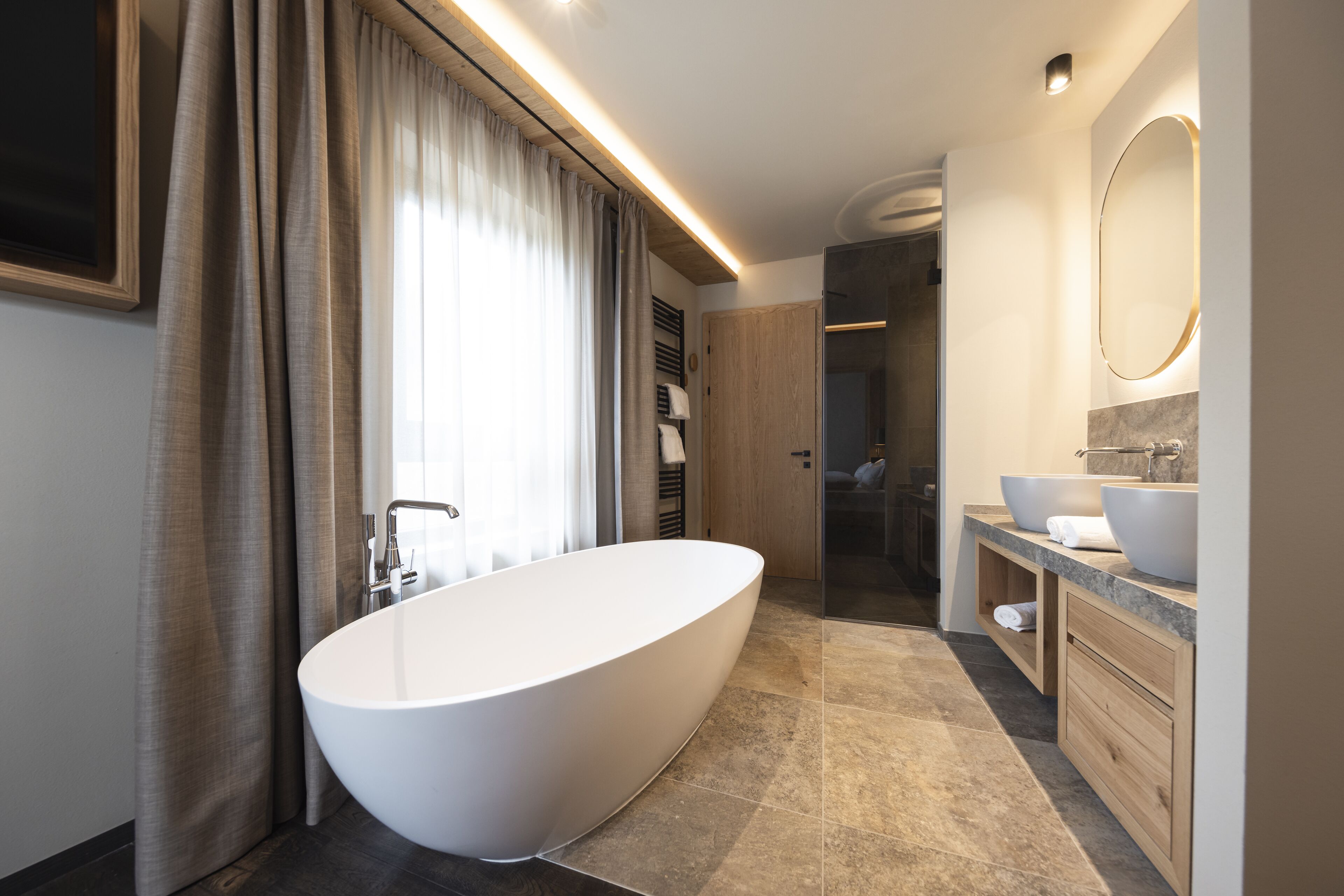 A modern bathroom with a freestanding bathtub, a large mirror, and a vanity with two sinks.
