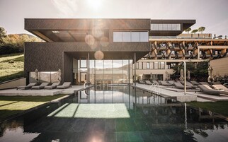 Un edificio moderno con piscina, sillones de descanso y vistas a la montaña.