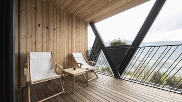 A wooden deck with two white cushioned chairs and a small table, overlooking a mountainous landscape.