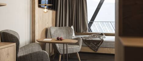 A cozy room with a wooden ceiling, a round table with a chair, a television, and a window with curtains.