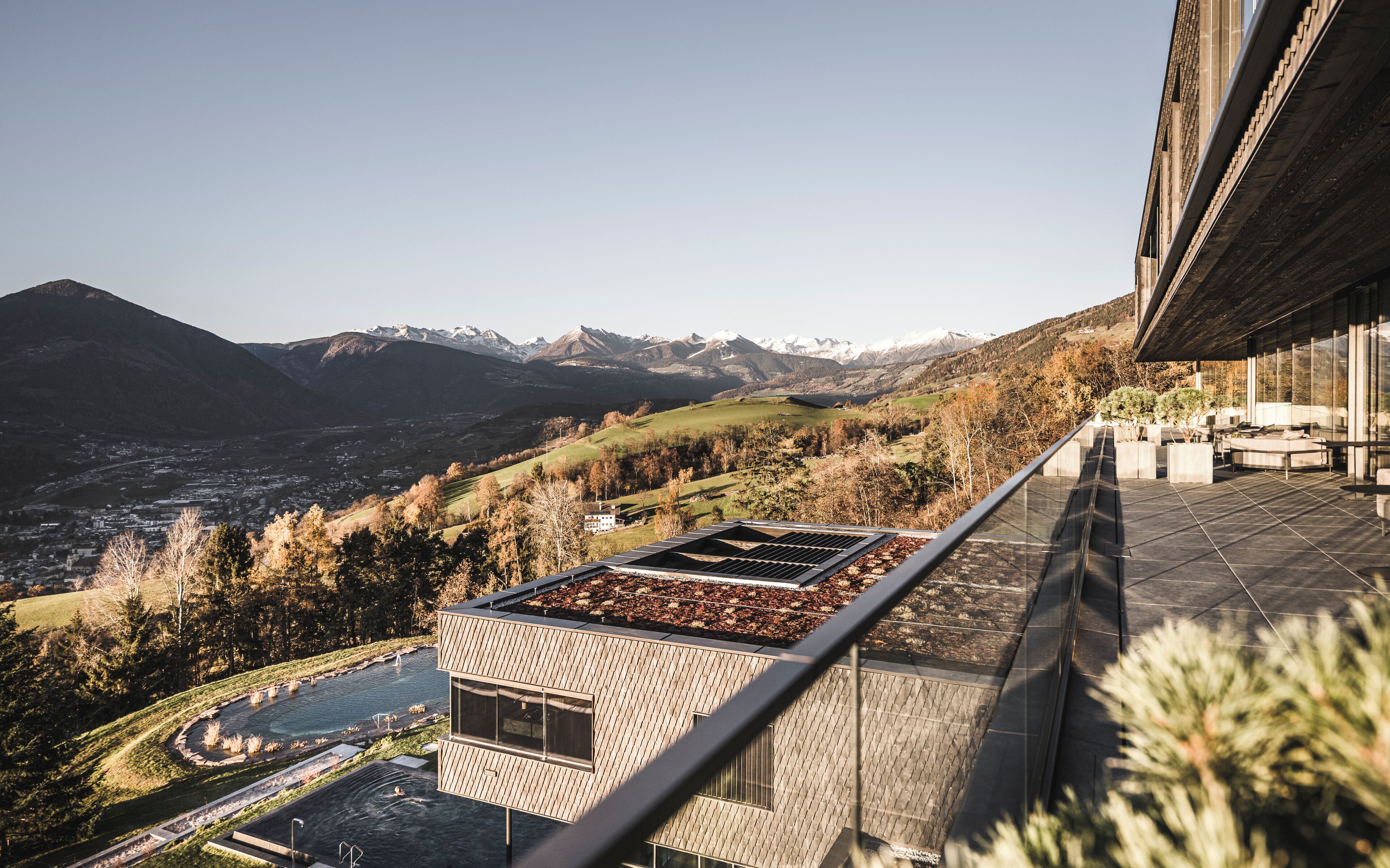 Un edificio moderno con jardín en la azotea y piscina, con vistas a un paisaje montañoso.