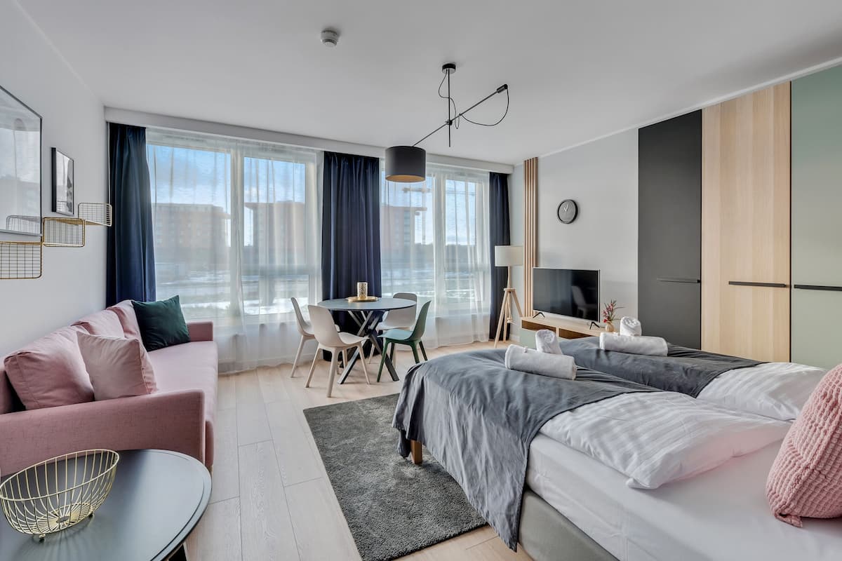 A modern hotel room with a bed, a sofa, a desk, and a TV.