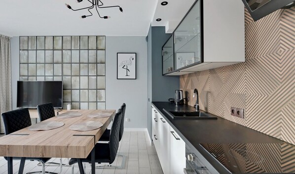 A modern kitchen with a wooden dining table, black chairs, a large window, and a patterned backsplash.