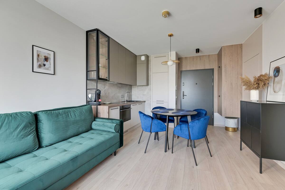 A modern kitchen with a dining area, a green sofa, and a small table with blue chairs.