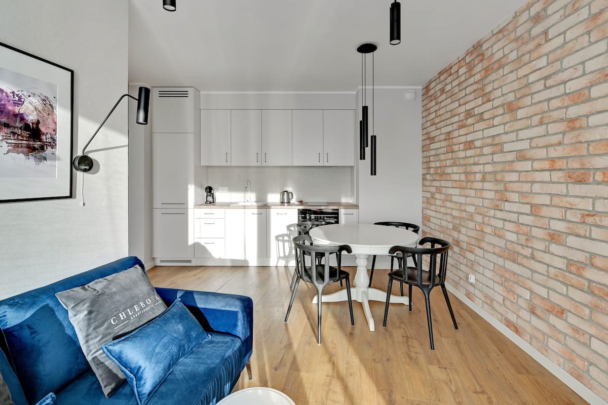 A modern kitchen with white cabinets, a dining table with chairs, and a blue sofa with a cushion.