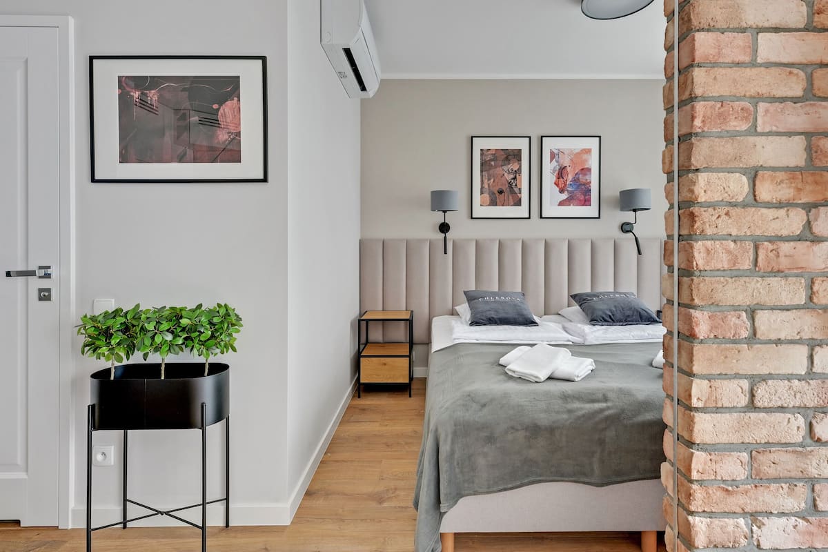 A modern bedroom with a bed, bedside lamps, a potted plant, and artwork on the wall.