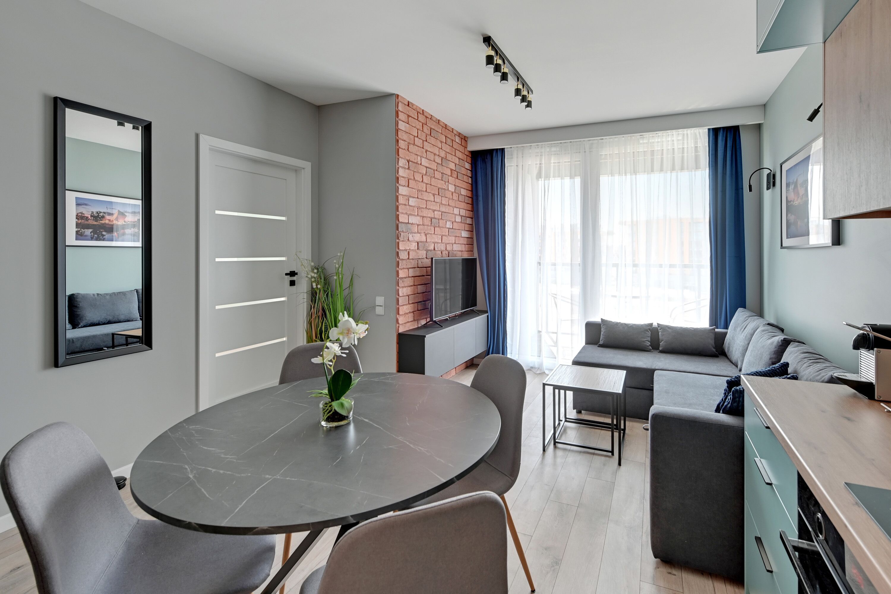 Una sala moderna con una mesa redonda de comedor, sofás grises y una pared de ladrillo decorativa.