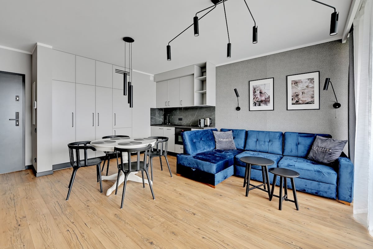 A modern kitchen with white cabinets, a marble countertop, and a blue velvet sofa with two black stools.