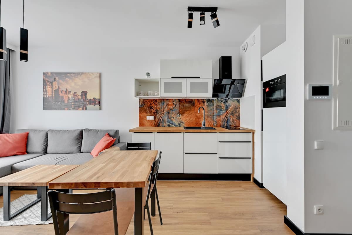 A modern kitchen with white cabinets, a wooden dining table, and a marble backsplash.