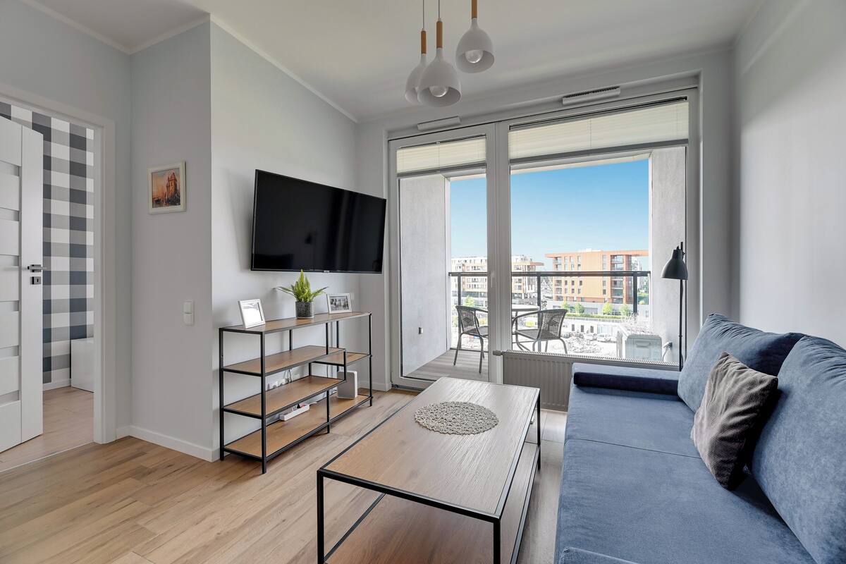 A modern living room with a sofa, a coffee table, a TV, and a large window with a city view.