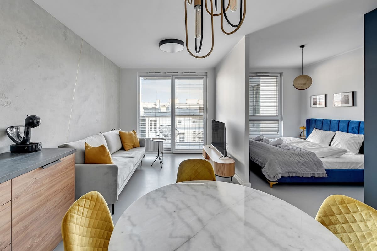 A modern apartment with a dining area, a sofa, a bed, and a TV.