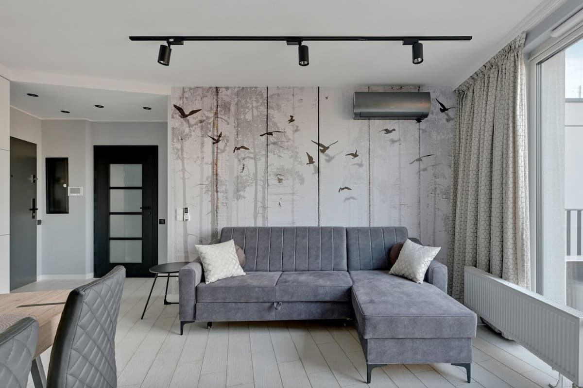 A modern living room with a grey sectional sofa, a small round table, and a wall with a bird mural.