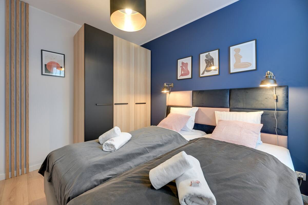 A modern hotel room with two beds, a large wardrobe, and artwork on the walls.