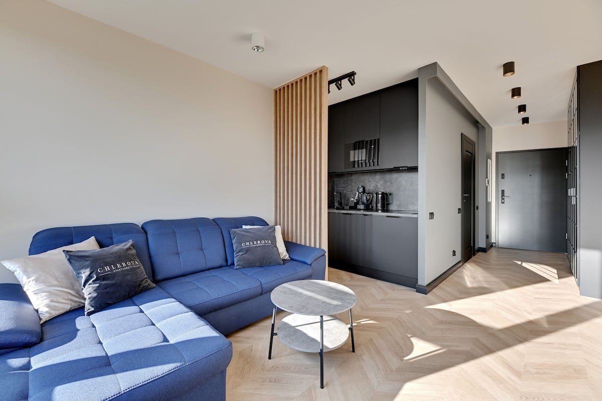 A modern living room with a blue sofa, a small round table, and a kitchen area in the background.