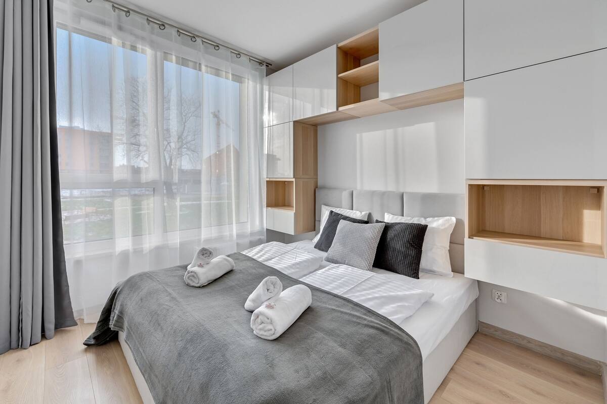 A modern hotel room with a large bed, built-in shelving, and a view of the outdoors.