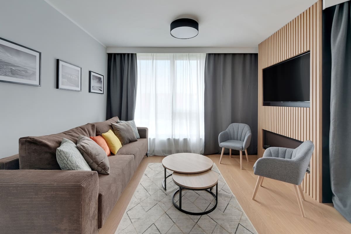 A modern living room with a sofa, two round coffee tables, a grey armchair, and a TV mounted on a wooden panel wall.