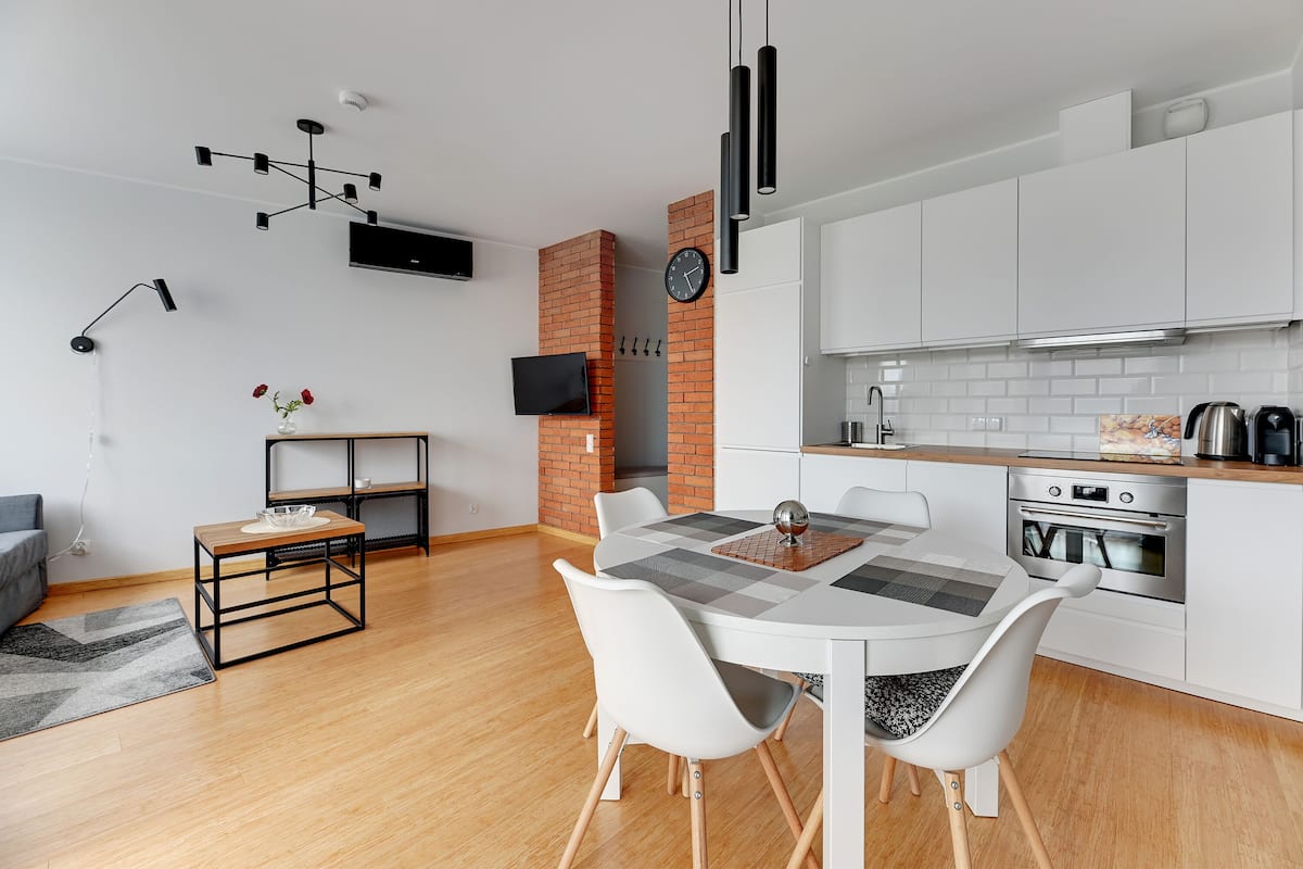 A modern kitchen with white cabinets, a built-in oven, and a dining area with a white table and chairs.