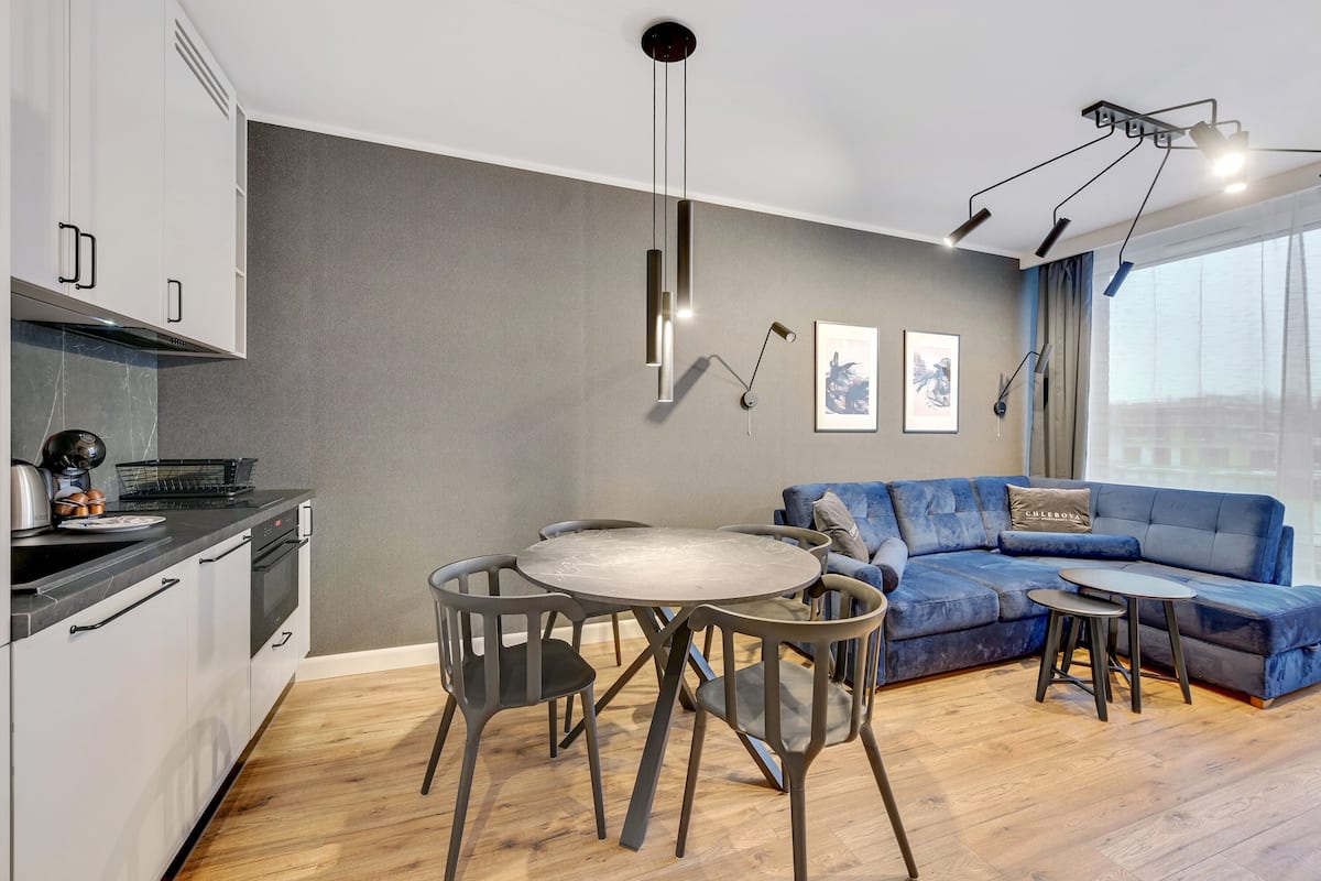 A modern living room with a round dining table, a sofa, and a kitchen area with cabinets and a stove.