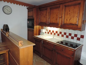 Een keuken met houten kastjes, een magnetron, een koffiezetapparaat en een klok aan de muur.