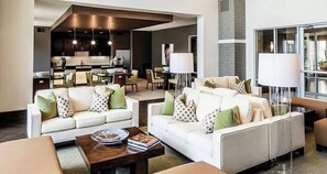 A modern living room with two sofas, a coffee table, and a dining area with chairs and a kitchen in the background.