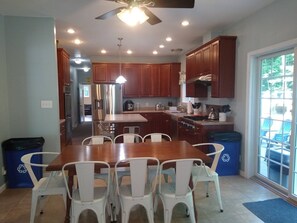 A spacious kitchen with wooden cabinets, a stainless steel refrigerator, and a dining area with a wooden table and white chairs.