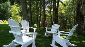 Dos sillas Adirondack blancas en un área verde rodeada de  árboles.
