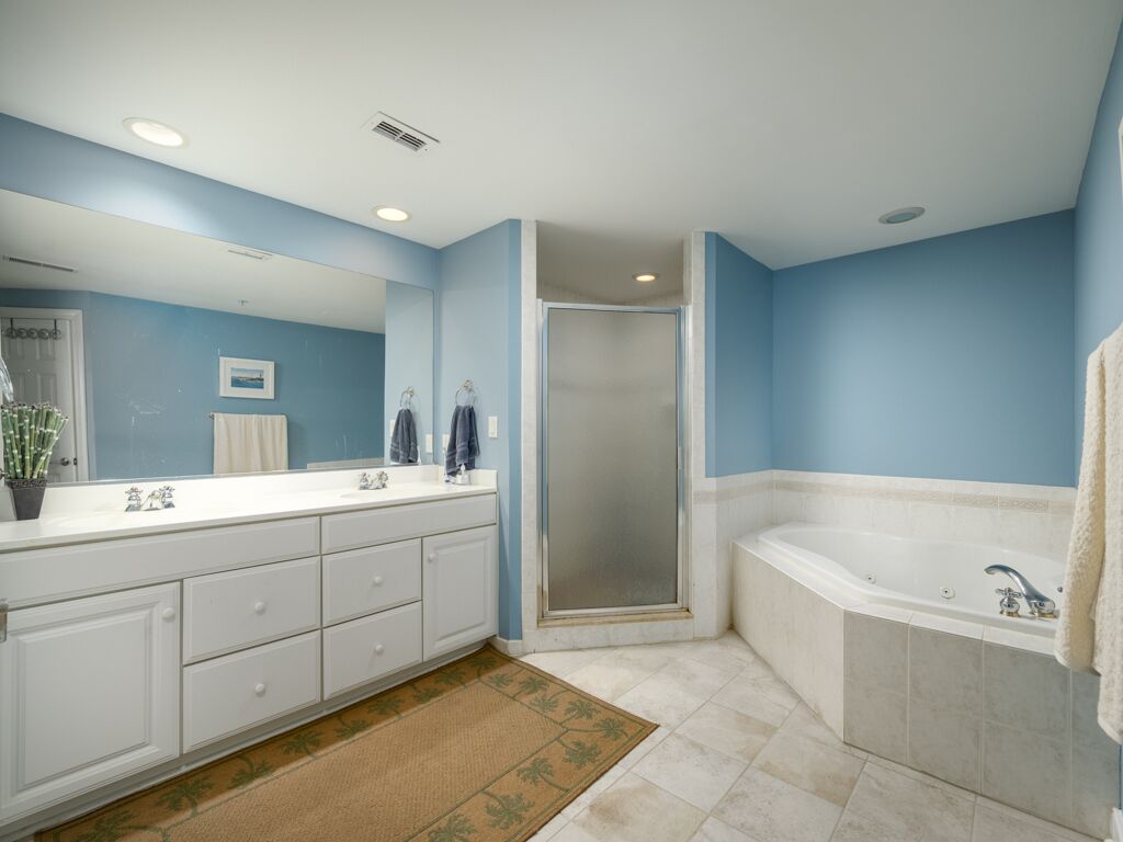 A bathroom with a large mirror, a shower, a bathtub, and a double vanity with drawers.