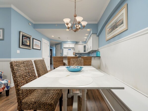 Un coin repas avec une table blanche, des chaises en osier et un saladier bleu.
