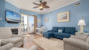 Una sala de estar con un sofá azul, dos sillones, una chimenea, un ventilador de techo y un televisor mostrando 'Central Reservations'.