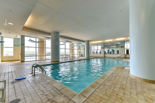 Una piscina interior con agua cristalina, suelo de baldosas y una escalera de natación.