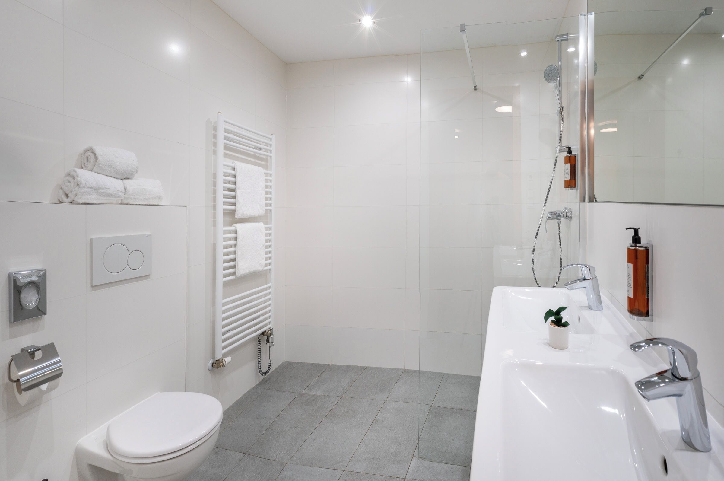 Un baño moderno con inodoro blanco, un lavamanos grande y una zona de ducha.